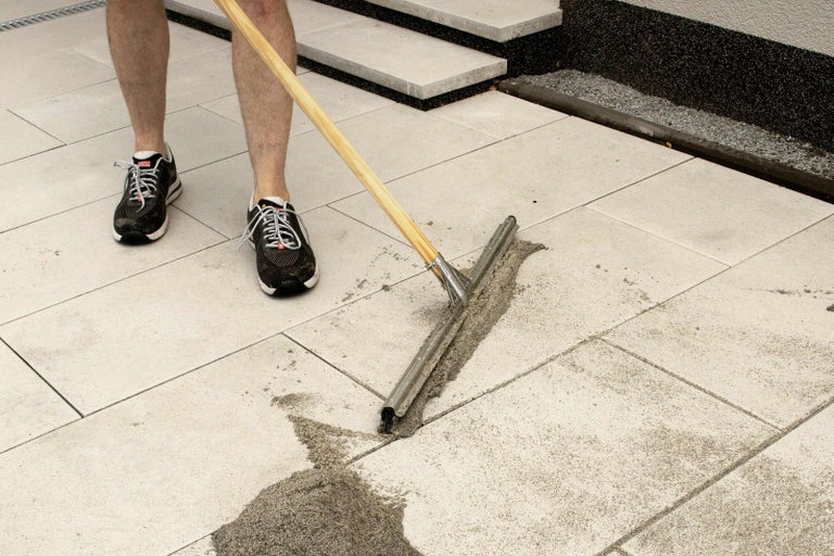Osoba zametá dlažební kostky s čističem spár a pískem