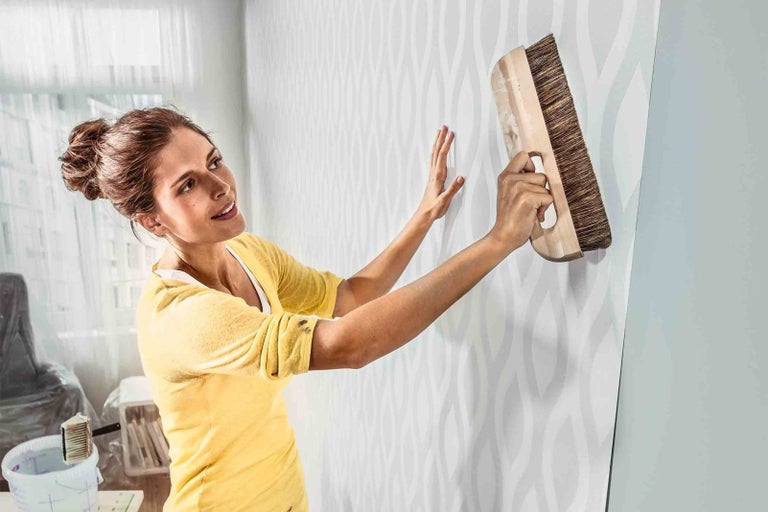 Žena tapetuje stěnu vzorem a tapetovacím kartáčem