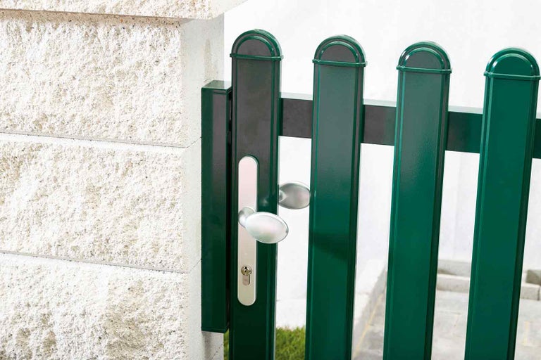 Detailní pohled na kovovou zahradní branku s klikou vedle zdi