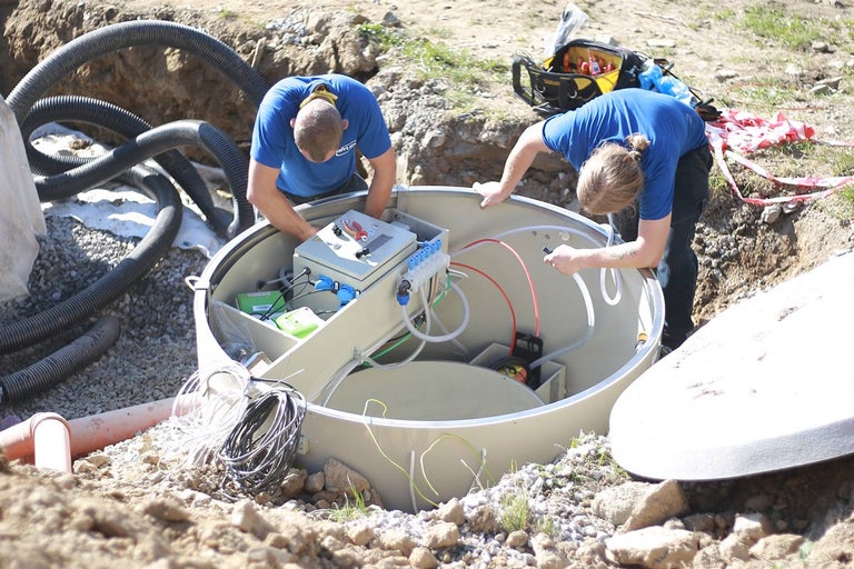 Dva pracovníci instalují venkovní čističku odpadních vod.