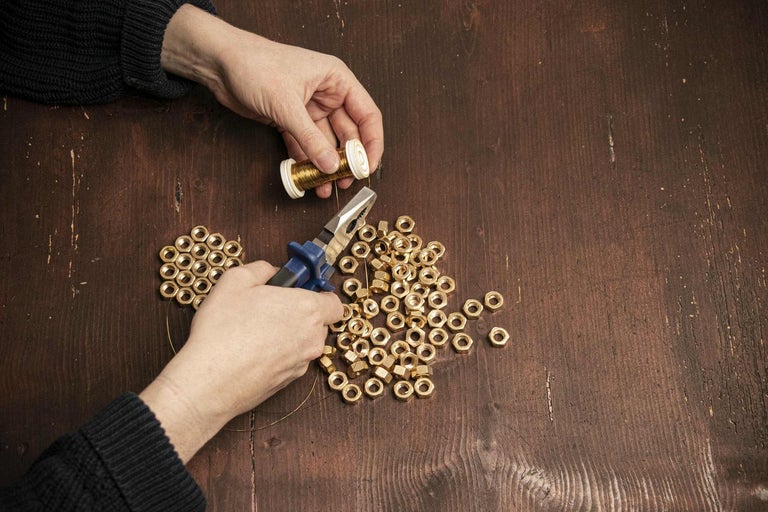 Osoba pracuje s maticemi, drátem a kleštěmi na dřevěném stole.
