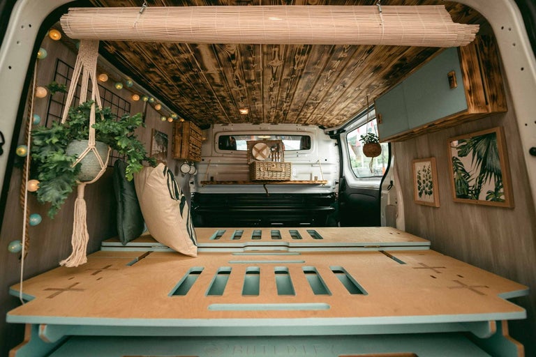 Interiér obytného vozu s dřevěnou postelí, obložením stropu a dekoracemi