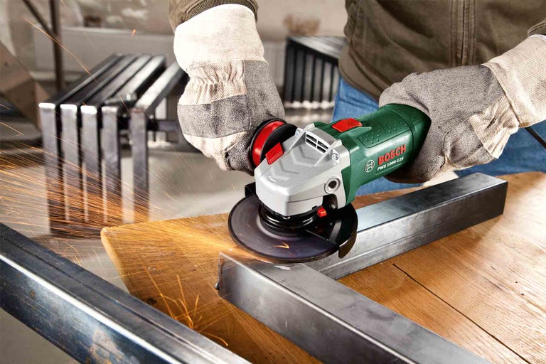 Osoba brousí úhlovou bruskou kus kovu na dřevěném povrchu; létají jiskry.