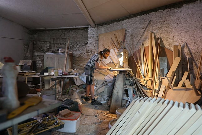 Muž pracuje s lupénkovou pilou v dílně s dřevěnými stěnami a nářadím