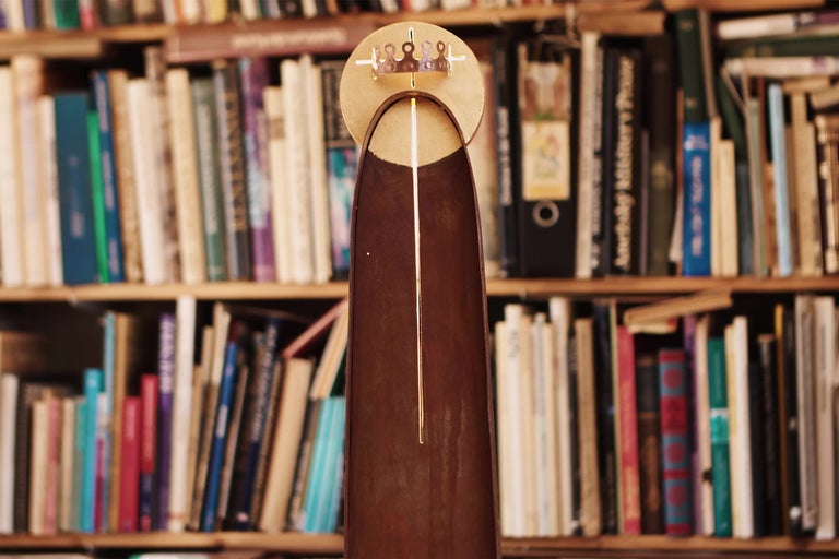 Dekorativní předmět s kruhovou hlavou a podlouhlým tělem před knihovnou