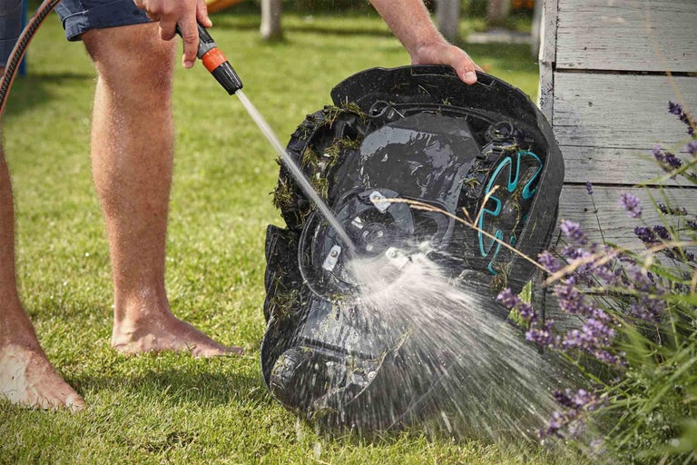 Osoba čistí robotickou sekačku hadicí venku.