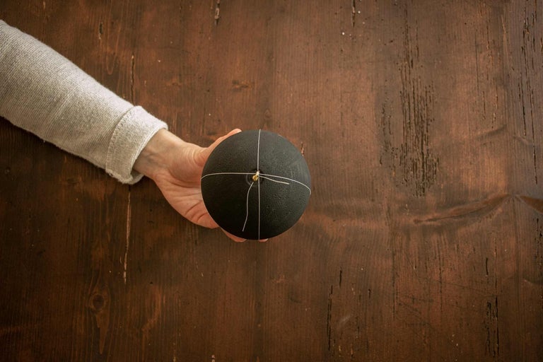 Ruka drží ozdobnou kouli s páskem na dřevěném stole