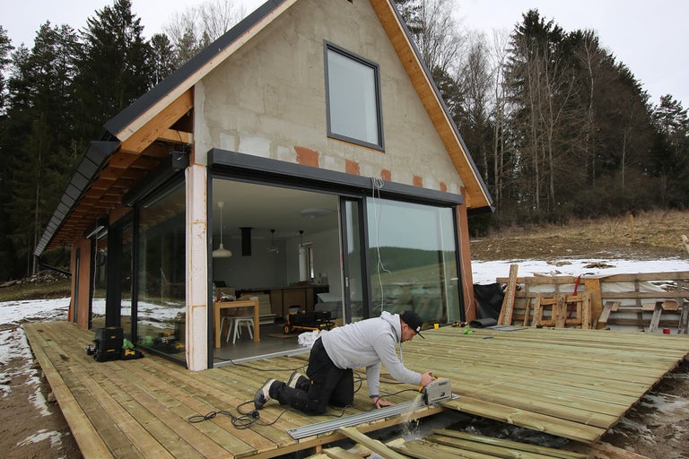 Muž řeže dřevěnou terasu u domu s posuvnými dveřmi