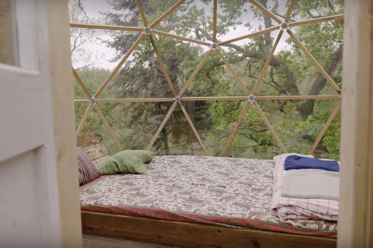 Vnitřní pohled na geodetický dřevěný dóm s postelí a výhledem na stromy
