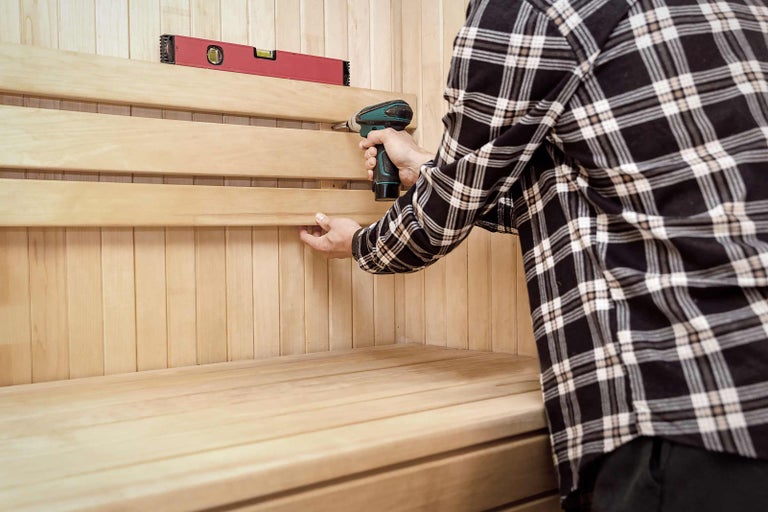 Muž montuje dřevěné panely v sauně pomocí akumulátorového šroubováku