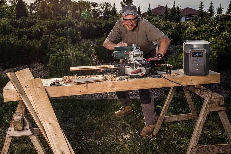 Muž řeže dřevo venku pomocí pokosové pily, napájené elektrárnou