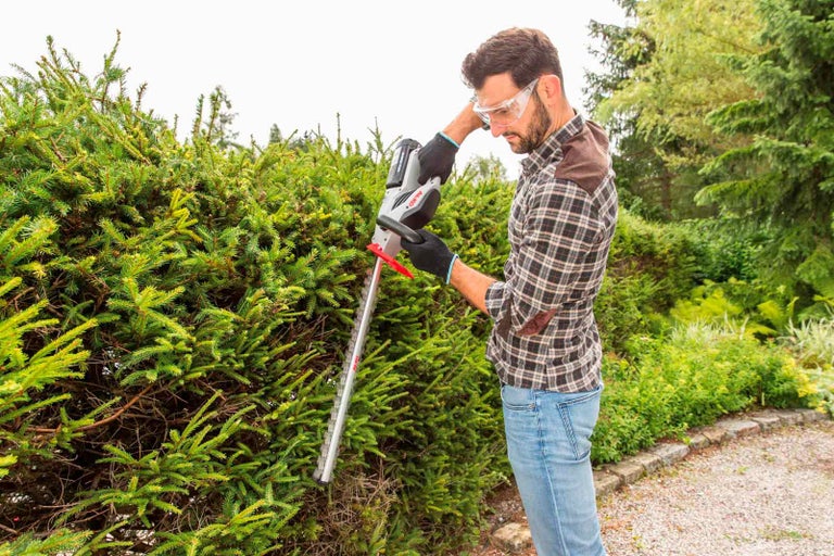 Muž stříhá živý plot akumulátorovými nůžkami na živý plot na zahradě.