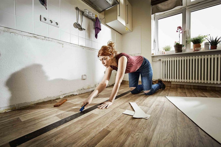 Žena pokládá podlahovou krytinu v kuchyni s nářadím