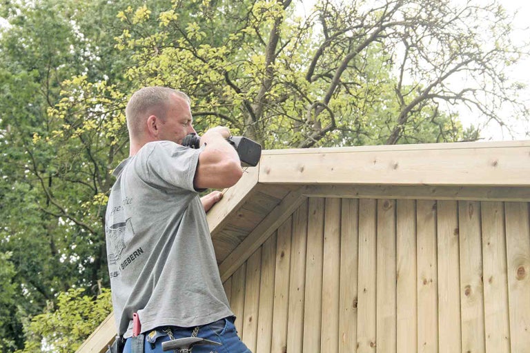 Řemeslník montuje dřevěnou fasádu pomocí akumulátorového šroubováku