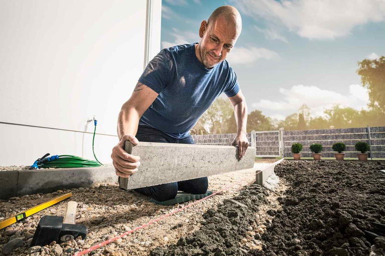 Muž pokládá obrubníky v zahradě.