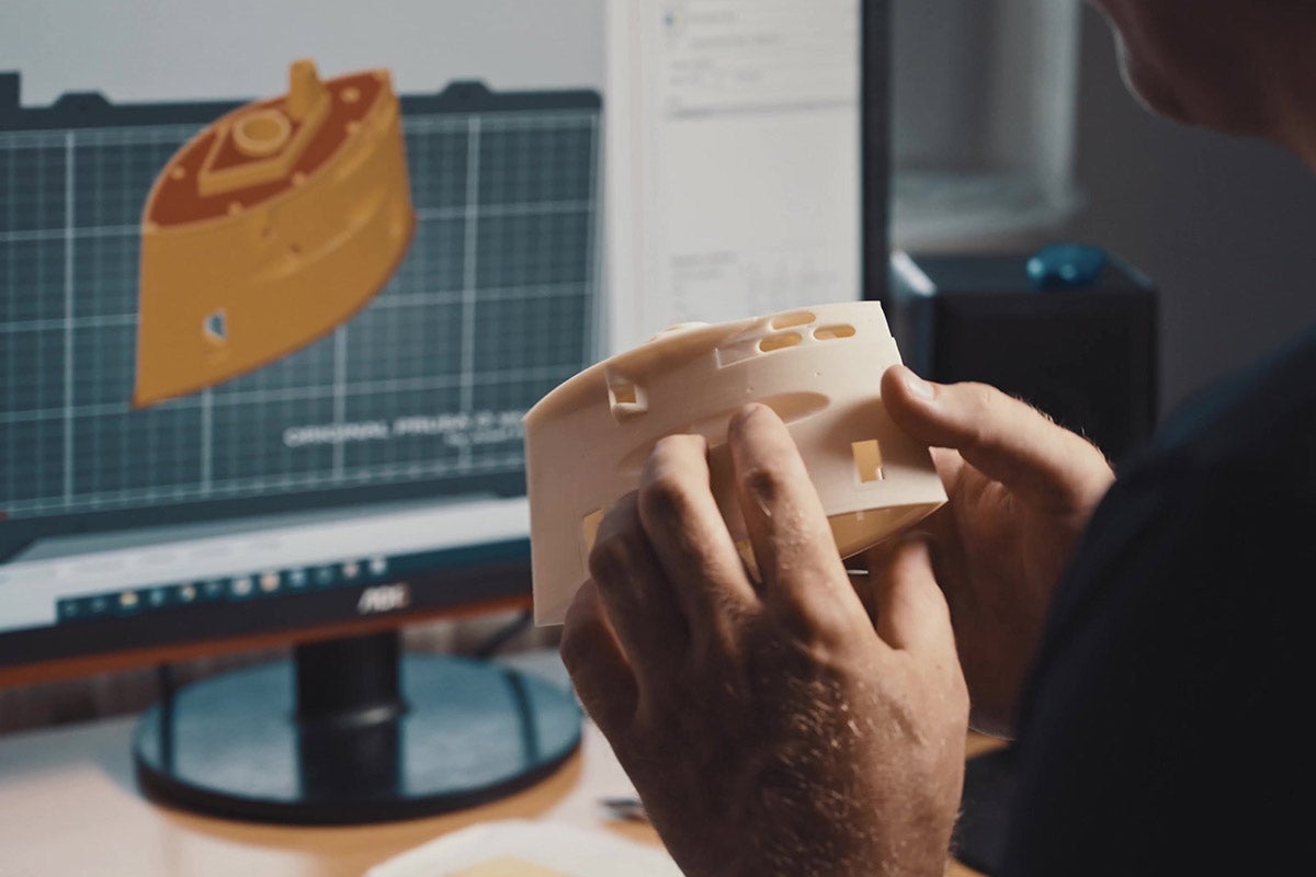 Muž drží 3D tištěný model před monitorem počítače