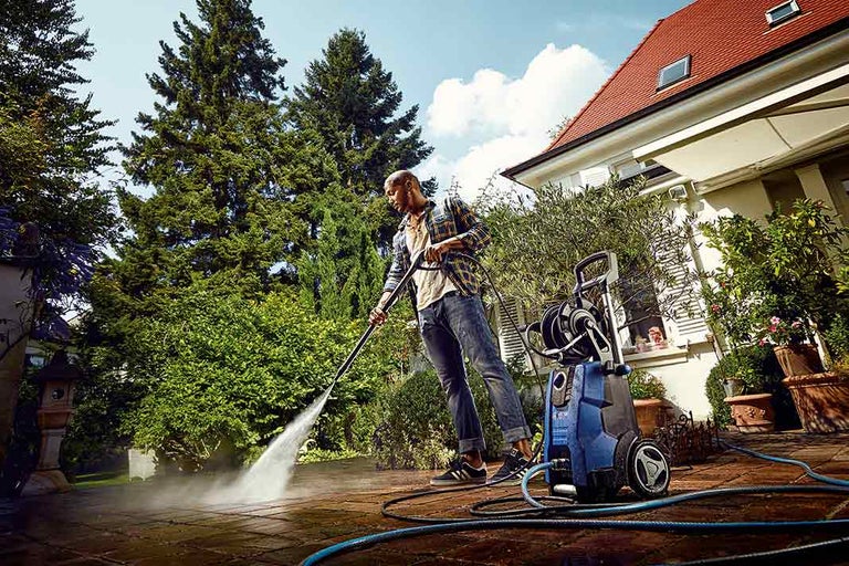 Muž čistí terasu vysokotlakým čističem na zahradě.