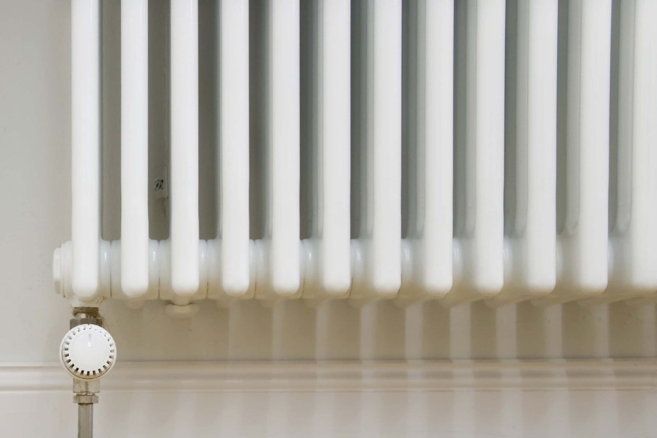 Bílý žebříkový radiátor s termostatem na zdi