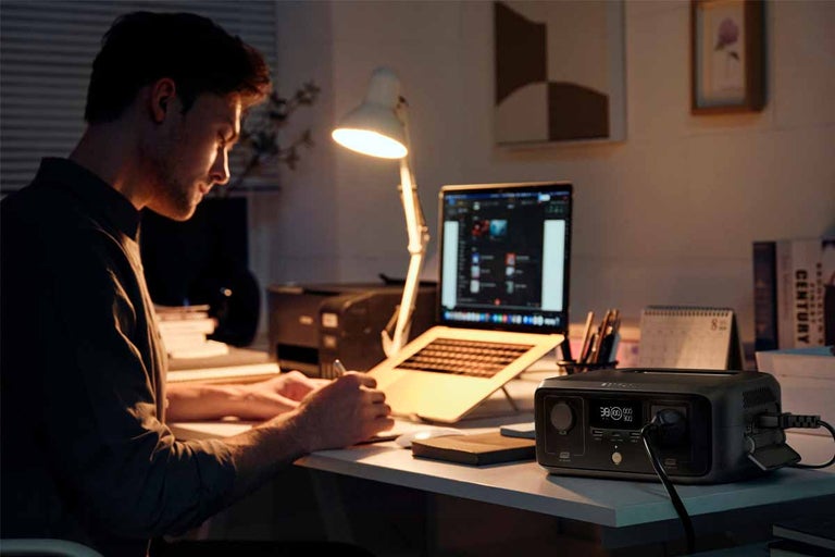 Přenosná elektrocentrála na stole v domácí kanceláři napájí notebook a stolní lampu.