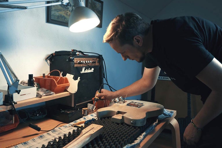 Muž pájí kytaru v dílně se zesilovačem a nářadím.