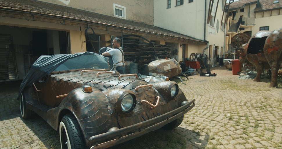 Mědí potažené auto stojí venku, částečně zakryté.