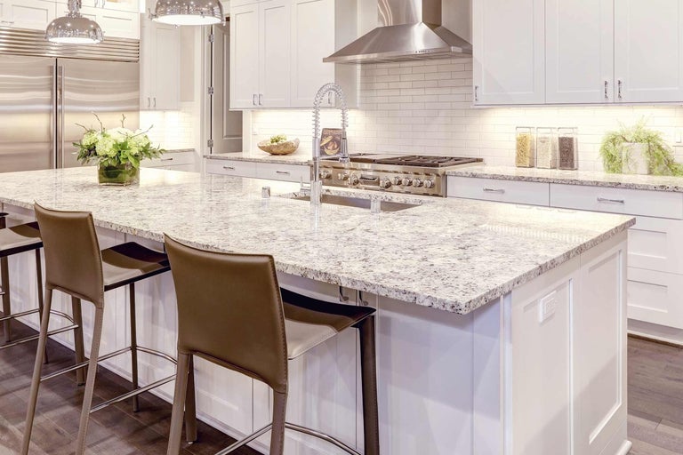 Světlá kuchyně s kuchyňským ostrovem, granitovou pracovní deskou, dřezem a barovými židlemi.