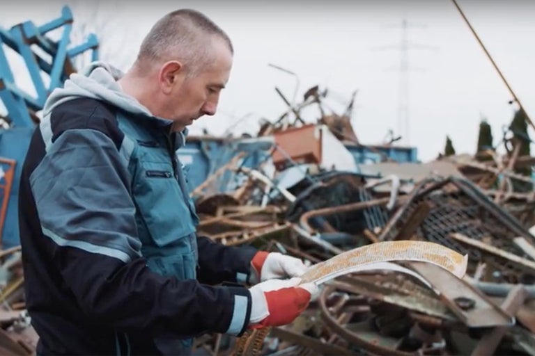 Muž s ochrannými rukavicemi kontroluje kovový díl před vrakovištěm