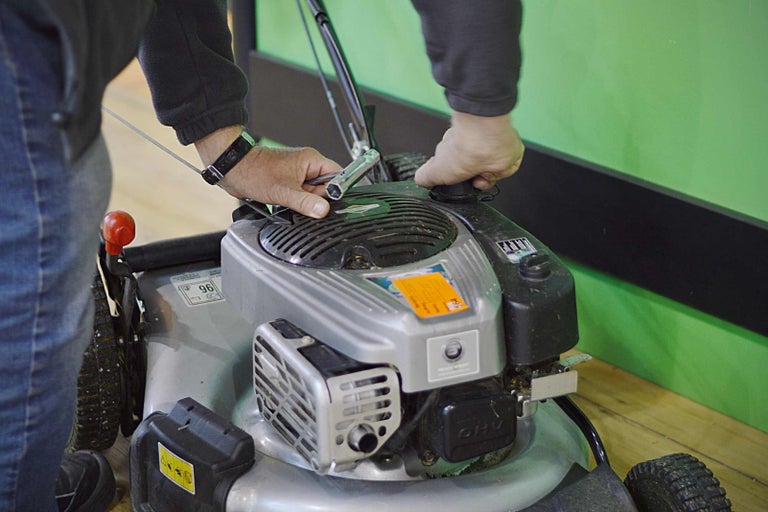 Osoba údržbuje seřizuje sekačku na trávu pomocí klíče.