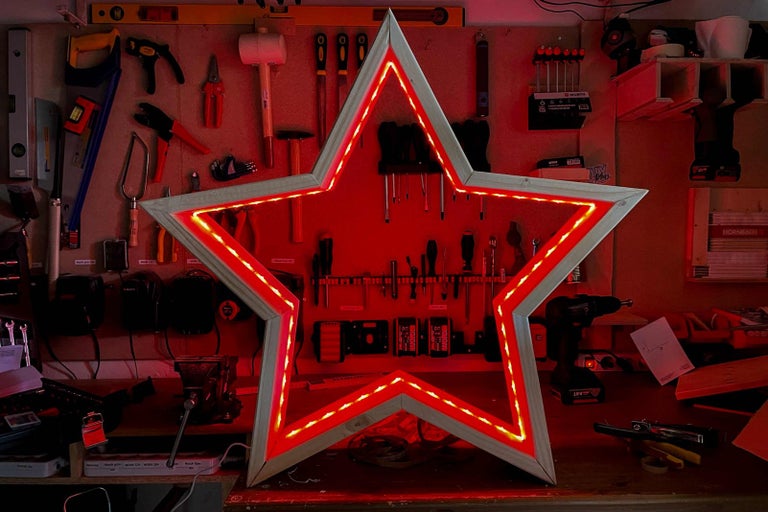 Dekorativní dřevěná hvězda s červeným LED osvětlením před stěnou s nářadím