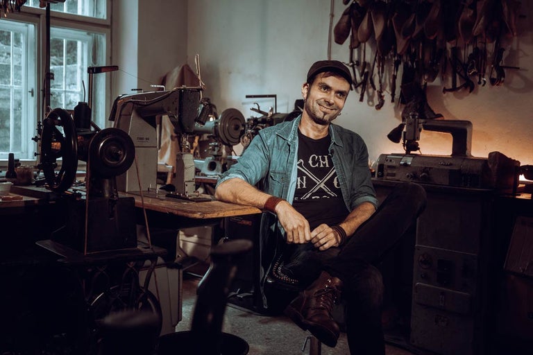 Muž sedí v dílně se šicími stroji a koženými nástroji