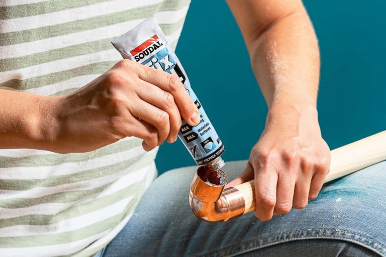 Uživatel nanáší lepidlo z tuby Soudal Fix All na měděnou trubku