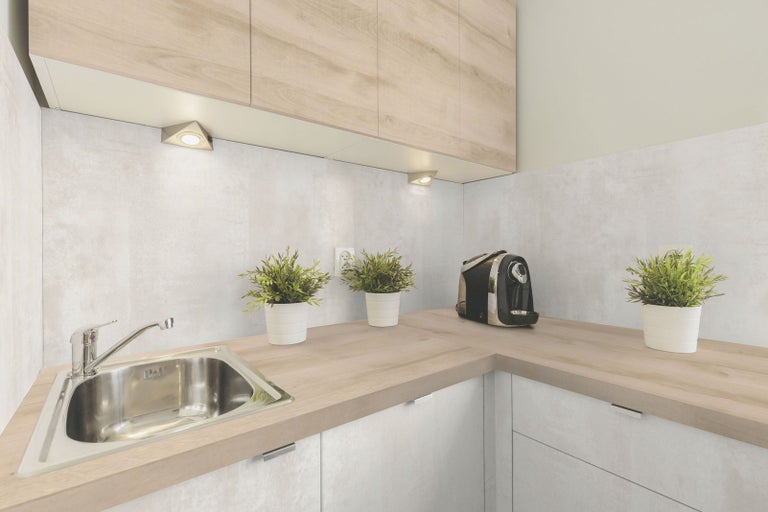 Světlá kuchyně s dřezem, pracovní deskou, kuchyňskými skříňkami a dekorací