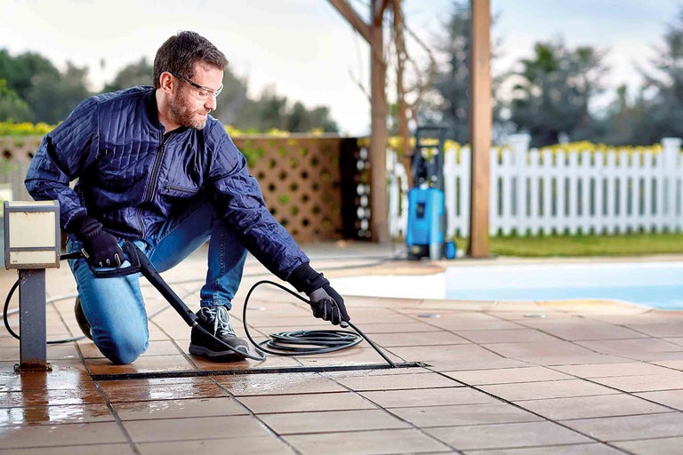 Muž čistí terasové spáry vysokotlakým čističem venku