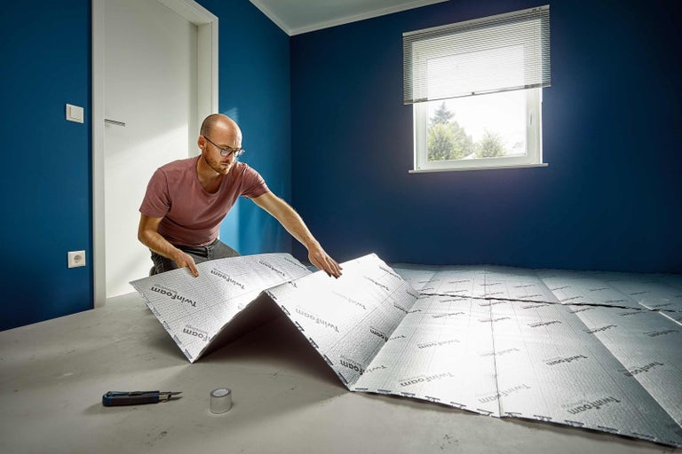 Muž pokládá izolační desky na podlahu v místnosti.