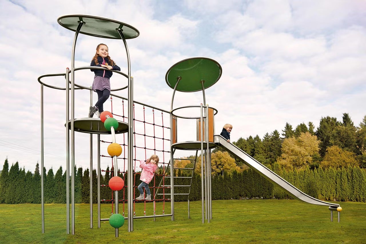 Hřiště se skluzavkou, horolezeckou sítí a dětmi na zeleném trávníku