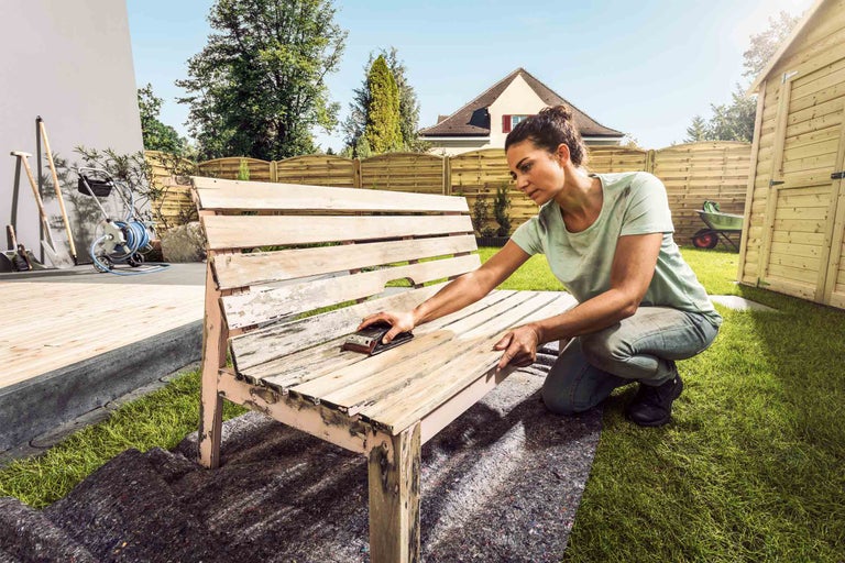 Žena brousí zahradní lavici venku.