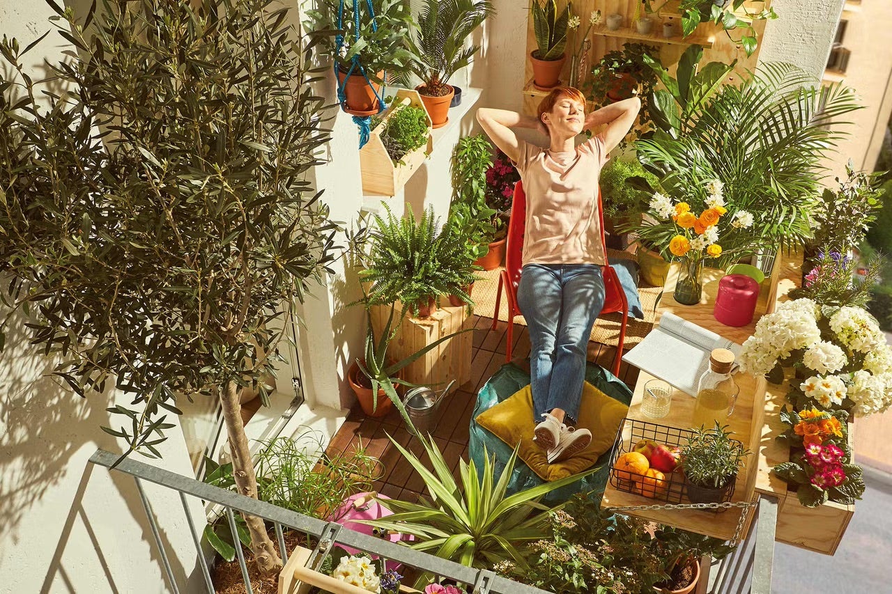 Žena relaxuje na balkoně s rostlinami v květináčích, bednách a závěsných květináčích.