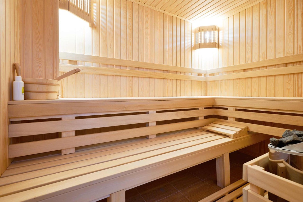 Světlá dřevěná sauna s lavicemi, vědrem a naběračkou