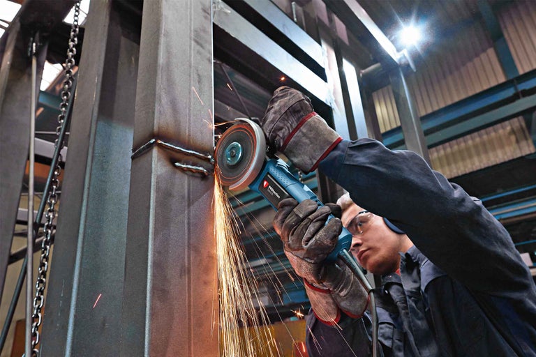 Muž brousí kov úhlovou bruskou v dílně, létají jiskry.
