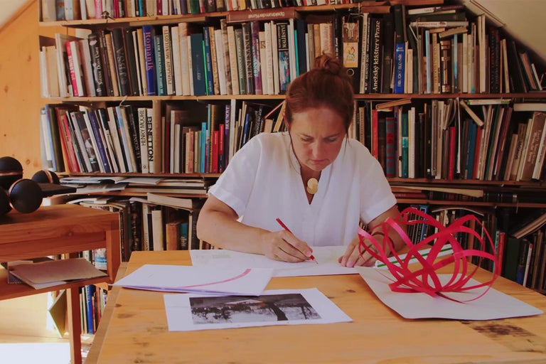 Žena sedí u stolu s knihami a navrhuje projekt