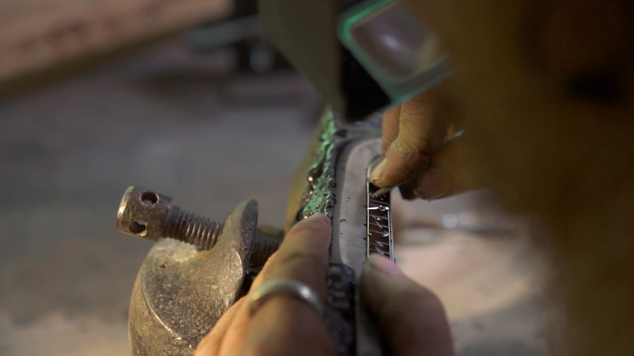 Detailní záběr pracovníka, který opracovává obrobek pomocí šroubovací svorky.