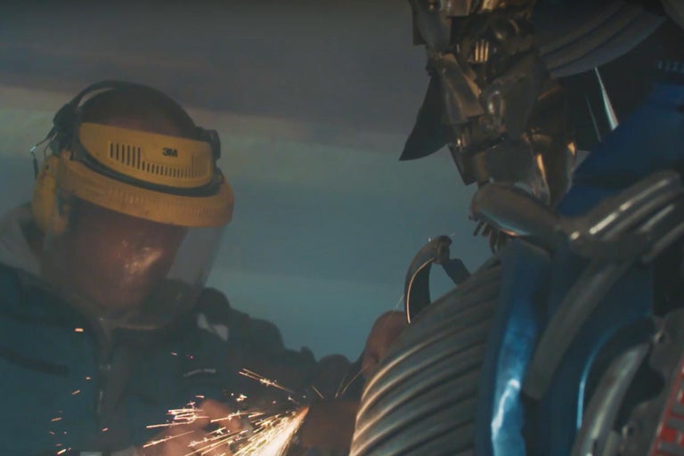 Muž s ochrannou přilbou brousí kov s jiskrami