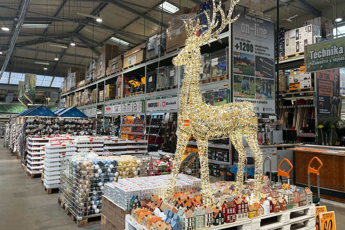 Ozdobný zlatý jelen v prodejně Hornbach, obklopený vánočními ozdobami a miniaturními domky.