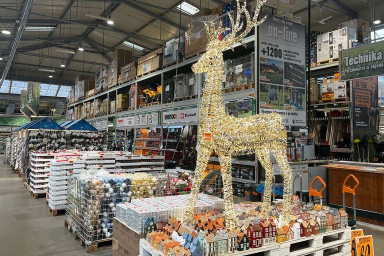 Ozdobný zlatý jelen v prodejně Hornbach, obklopený vánočními ozdobami a miniaturními domky.