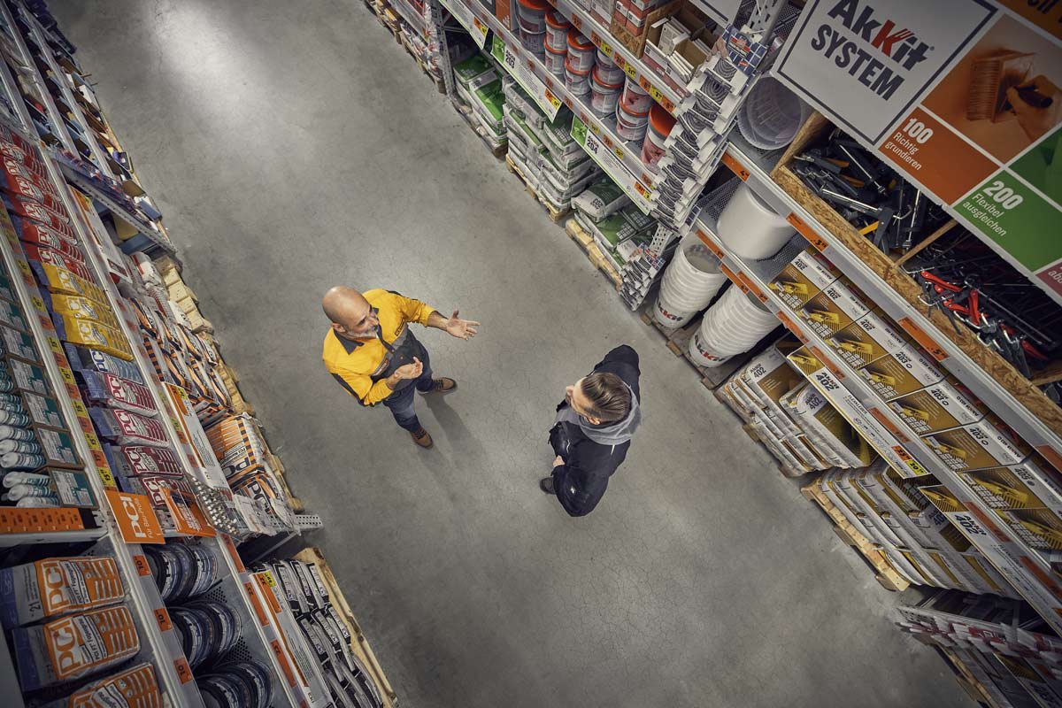 Pohled shora na uličku v hobbymarketu Hornbach s regály a dvěma osobami