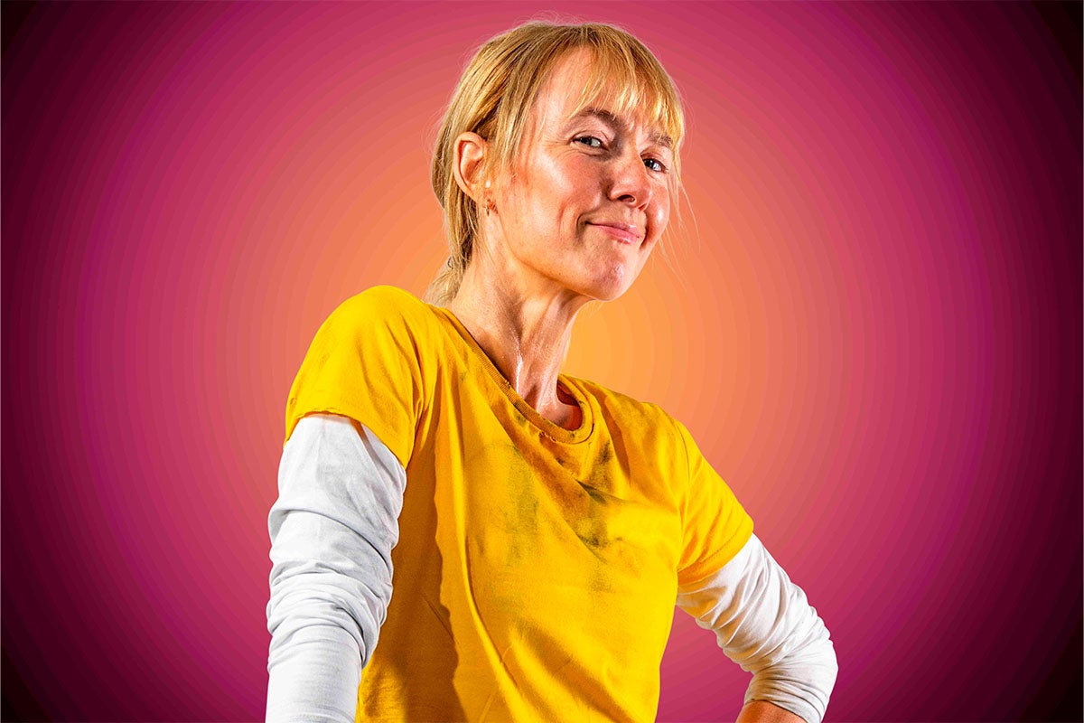 Žena se žlutým tričkem a bílým spodním tričkem pózuje před barevným pozadím.