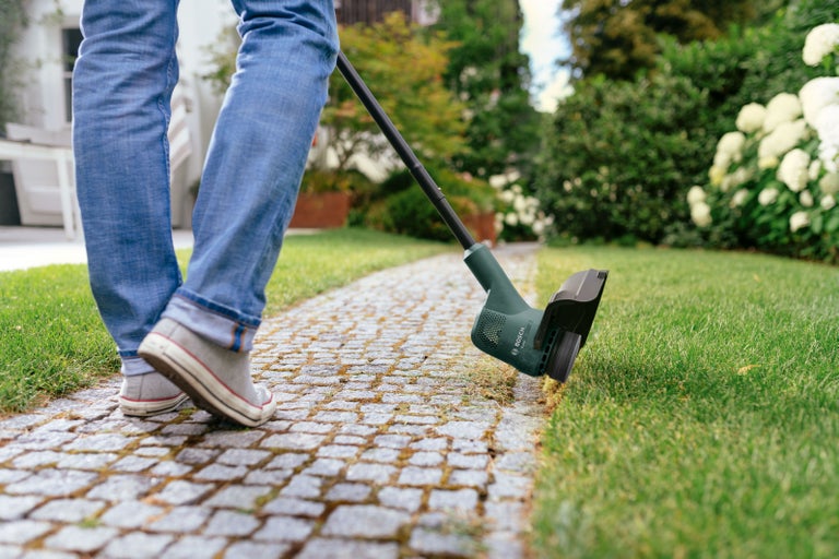 Zastřihovač okrajů trávníku v provozu na chodníku