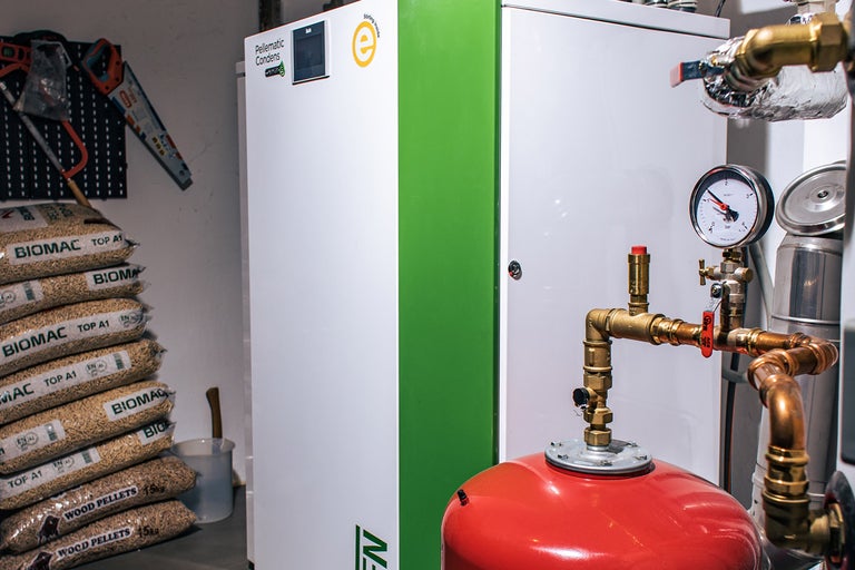 Peletové topení vedle pytlů s dřevěnými peletami, tlakoměru a nářadí na zdi.