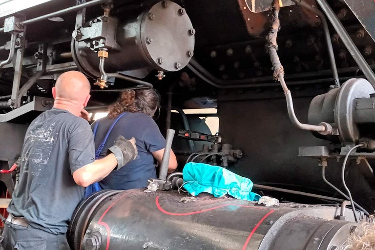 Interiér parní lokomotivy se dvěma lidmi provádějícími údržbu