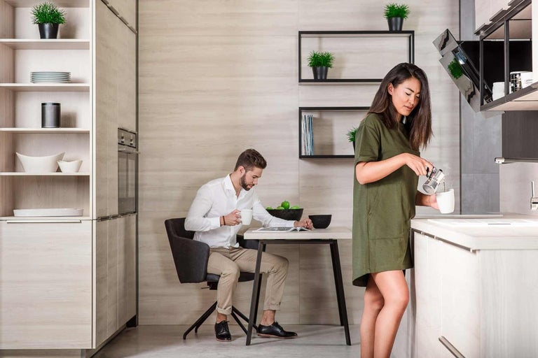 Světlá kuchyně s mužem u stolu a ženou, která připravuje kávu